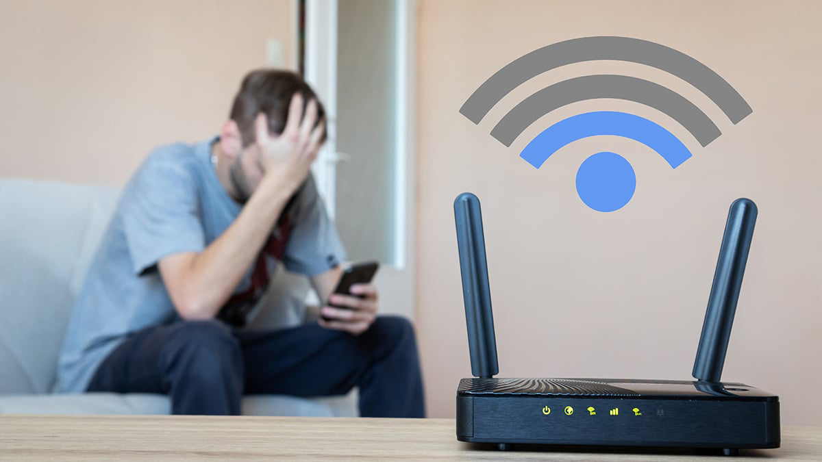 An angry man looking at his phone with a router nearby showing only 2 bars.
